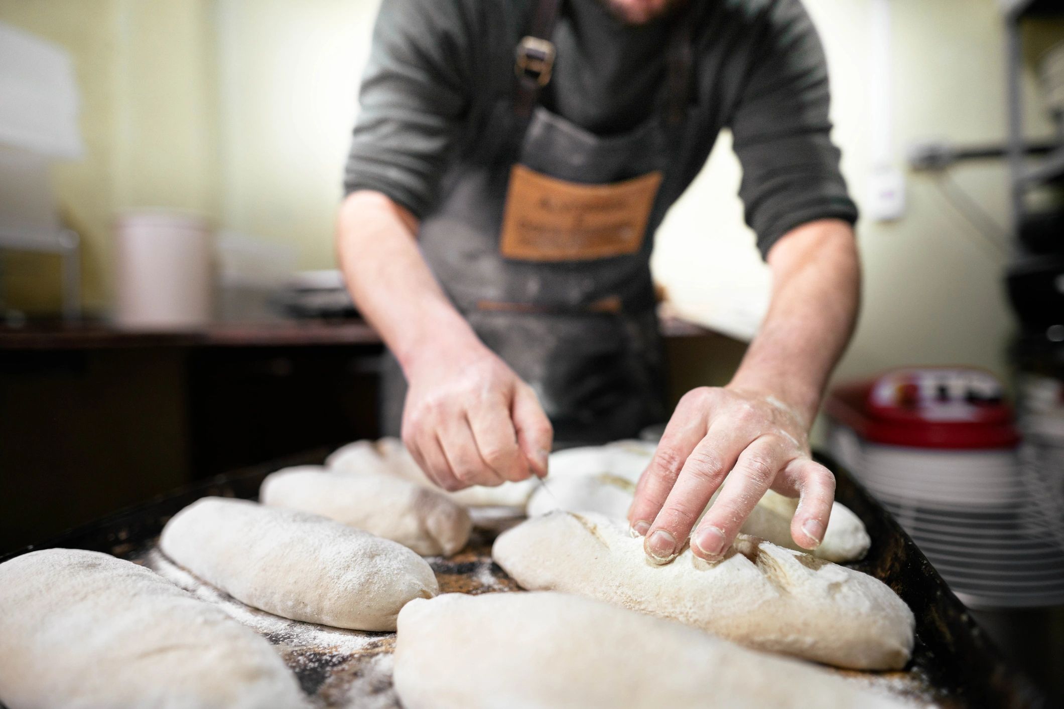 Baker scoring loaves of bread before baking.