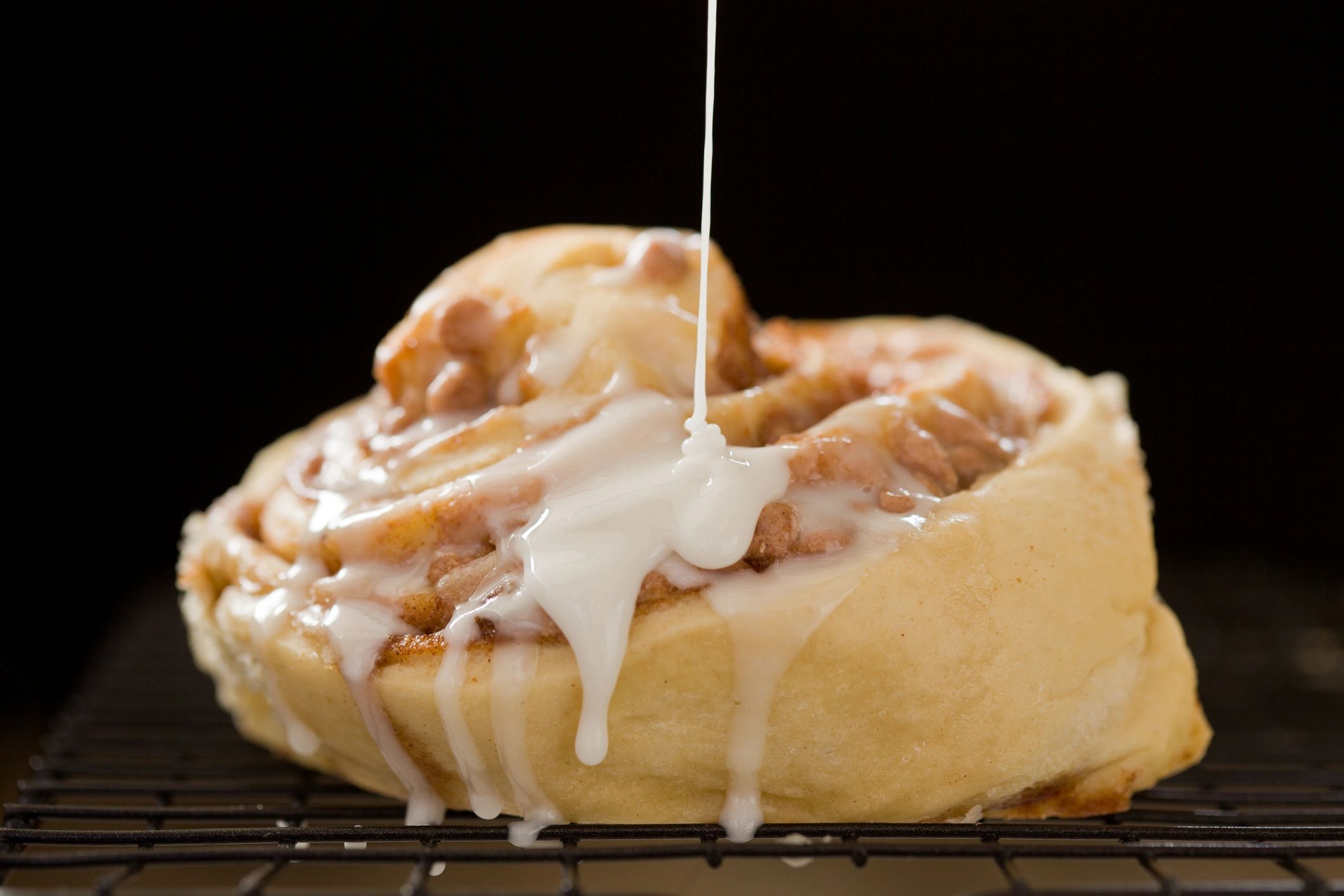 Icing being drizzled over a cinnamon roll on a cooling rack